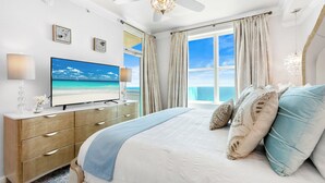 A bedroom with a large bed, a television, a ceiling fan, and a view of the ocean.