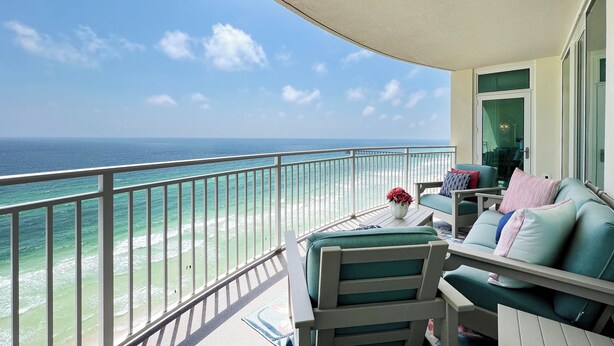 A balcony with a view of the ocean, a seating area with a sofa and chairs, and a small table with a vase.