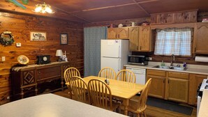 A wooden cabin interior with a dining table, chairs, a refrigerator, a microwave, wooden cabinets, and a window with curtains. - Beautiful Log Cabin. Sleeps 2-8. Reds Landing boat ramp .5 mi away. A+ fishing. (Norfork)