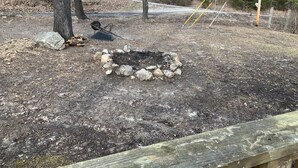 A campsite with a fire pit surrounded by rocks, a metal chair, and a wooden bench. - Beautiful Log Cabin. Sleeps 2-8. Reds Landing boat ramp .5 mi away. A+ fishing. (Norfork)