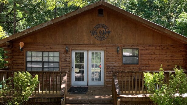 A wooden cabin with a front porch, two doors, and a logo above the entrance. - Beautiful Log Cabin. Sleeps 2-8. Reds Landing boat ramp .5 mi away. A+ fishing. (Norfork)