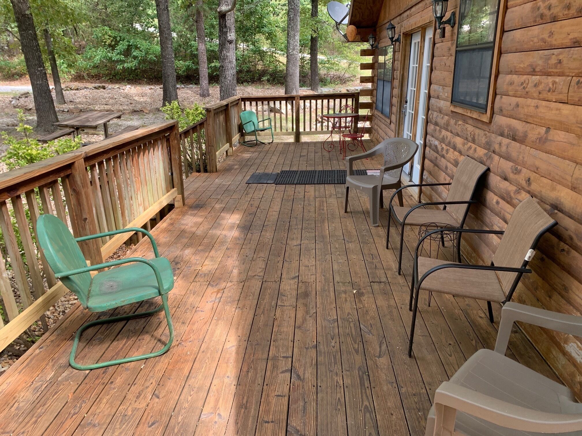A wooden deck with outdoor seating, including chairs and a table, surrounded by trees.