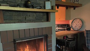 A fireplace with a stone wall backdrop, a kitchen area with a stove and a patterned plate, and a hanging rack with items. - White Mountain Four Season Vacation Getaway!! (Lincoln)