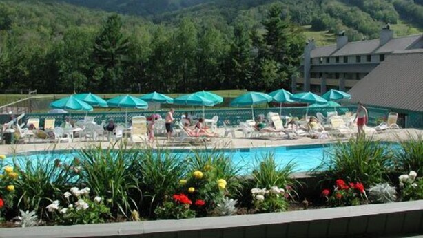 A pool area with lounge chairs and umbrellas, surrounded by greenery and mountains in the background. - White Mountain Four Season Vacation Getaway!! (Lincoln)