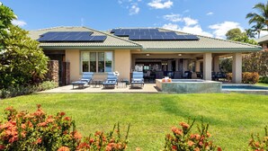 Une maison dotée d’un patio couvert, de panneaux solaires, d’une piscine et d’une pelouse bien entretenue.