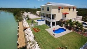 Una casa de dos pisos con piscina, muelle y vista al agua.
