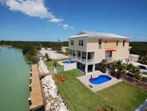 A two-story house with a pool, a dock, and a view of the water.