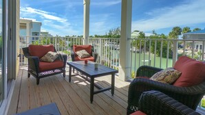 Un espacio al aire libre techado con mobiliario de mimbre y una mesa, con vista a una zona residencial con casas y vegetación.
