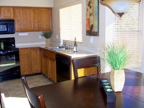 Una cocina con armarios de madera, microondas, horno, lavavajillas, un fregadero y una mesa de comedor con sillas.