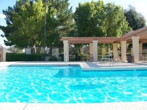 Una piscina con agua azul cristalina, rodeada por un porche cubierto con sillas y mesas.