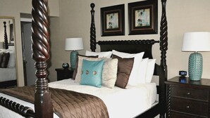 A four-poster bed with a dark wooden headboard, white bedding, and decorative pillows. There are two bedside tables with lamps and a clock. The room has a neutral color scheme and artwork on the walls. - Well Maintained, Super Clean, and Perfect Location (Peoria)