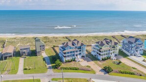 A coastal residential area with beachfront properties, including a multi-story building with balconies and a separate tower-like structure. - Premier Oceanfront w Pool, Hot Tub, Elevator, Theater, Game Room, Outdoor Lounge (Hatteras)