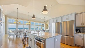 A spacious kitchen with a large island, stainless steel appliances, and a view to the ocean. - Premier Oceanfront w Pool, Hot Tub, Elevator, Theater, Game Room, Outdoor Lounge (Hatteras)