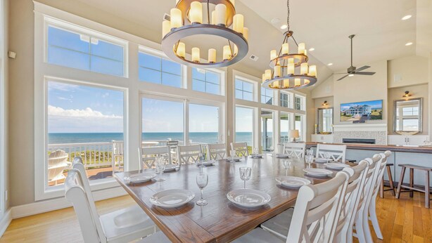 A spacious dining area with a view of the ocean, large windows, and modern chandeliers. - Premier Oceanfront w Pool, Hot Tub, Elevator, Theater, Game Room, Outdoor Lounge (Hatteras)
