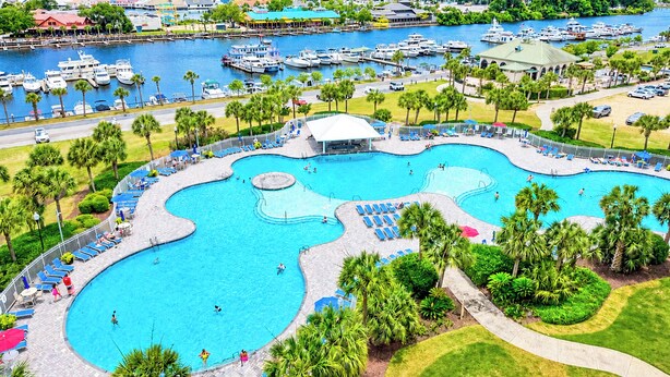 A large outdoor swimming pool with multiple sections, surrounded by palm trees and a marina with boats.