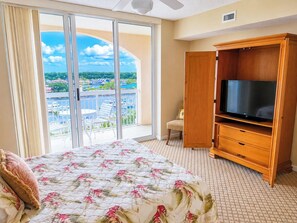 Ein Hotelzimmer mit einem Bett, einem Fernseher, einem Holzschrank und einer Glasschiebetür, die auf einen Balkon mit Blick auf einen Yachthafen führt.