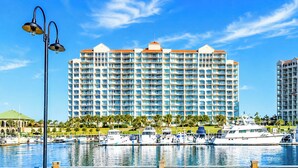 A waterfront hotel with multiple balconies, a marina with boats, and a clear blue sky.