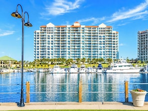 A waterfront hotel with multiple balconies, a marina with boats, and a clear blue sky.