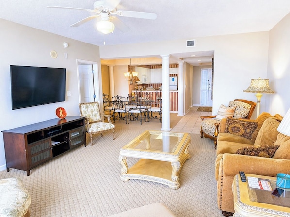 A living room with a flat-screen TV, a coffee table, a sofa, and a dining area with chairs and a chandelier.