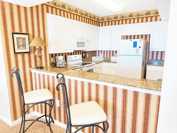 Eine Küche mit gestreifter Tapete, weißen Schränken, einer Arbeitsplatte, einem Herd, einem Kühlschrank und zwei Barhocker.
