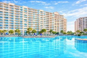 Un hotel con una piscina amplia, varios balcones y palmeras.
