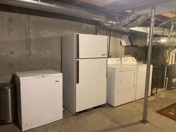 A laundry room with a washer and dryer, a compact refrigerator, and a metal trash can.