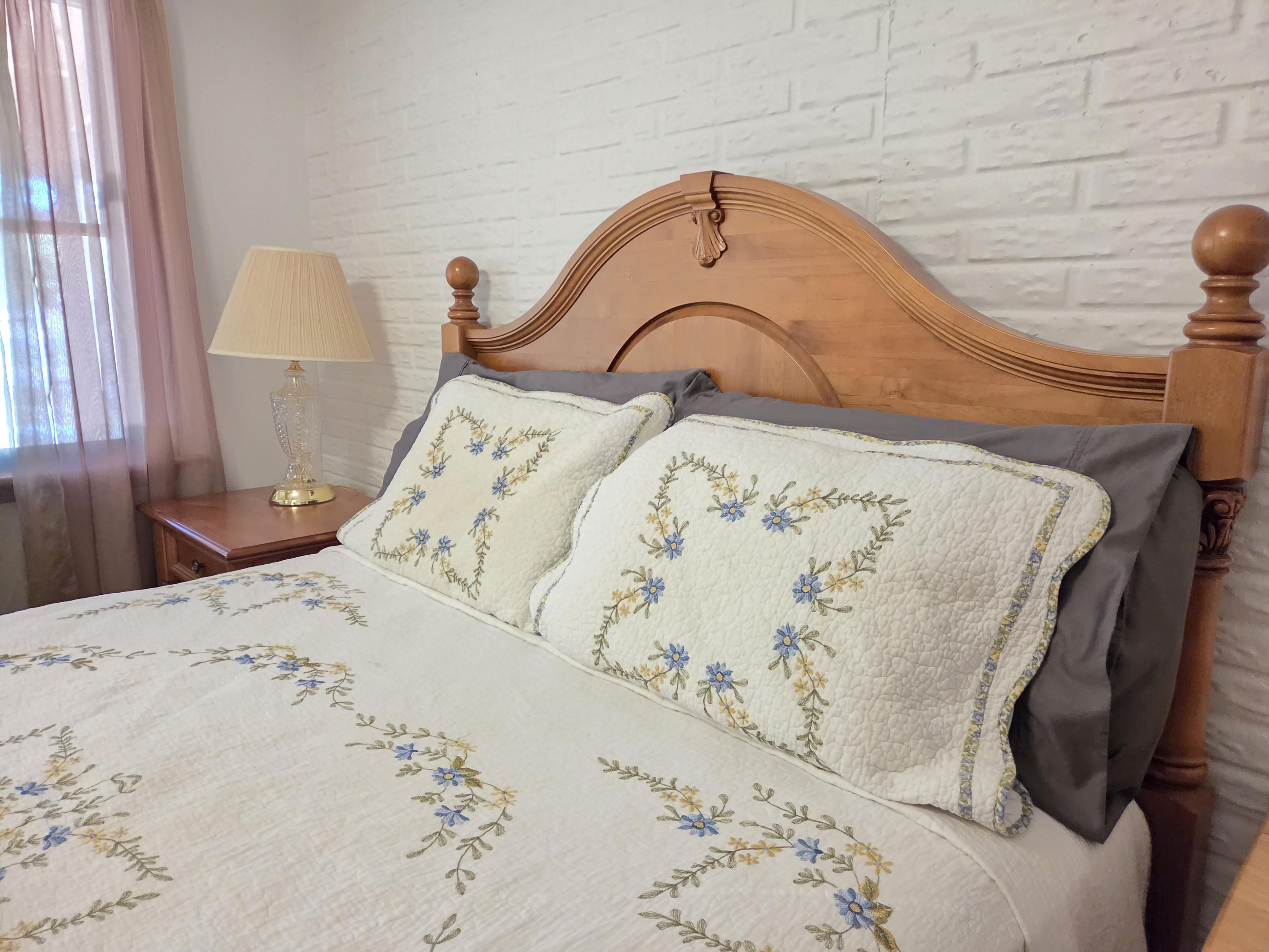 Un lit avec une courtepointe à motifs floraux, une tête de lit en bois et une table de chevet avec une lampe.