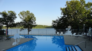 Ein Schwimmbecken mit Basketballkorb, Liegestühlen und Blick auf einen See.