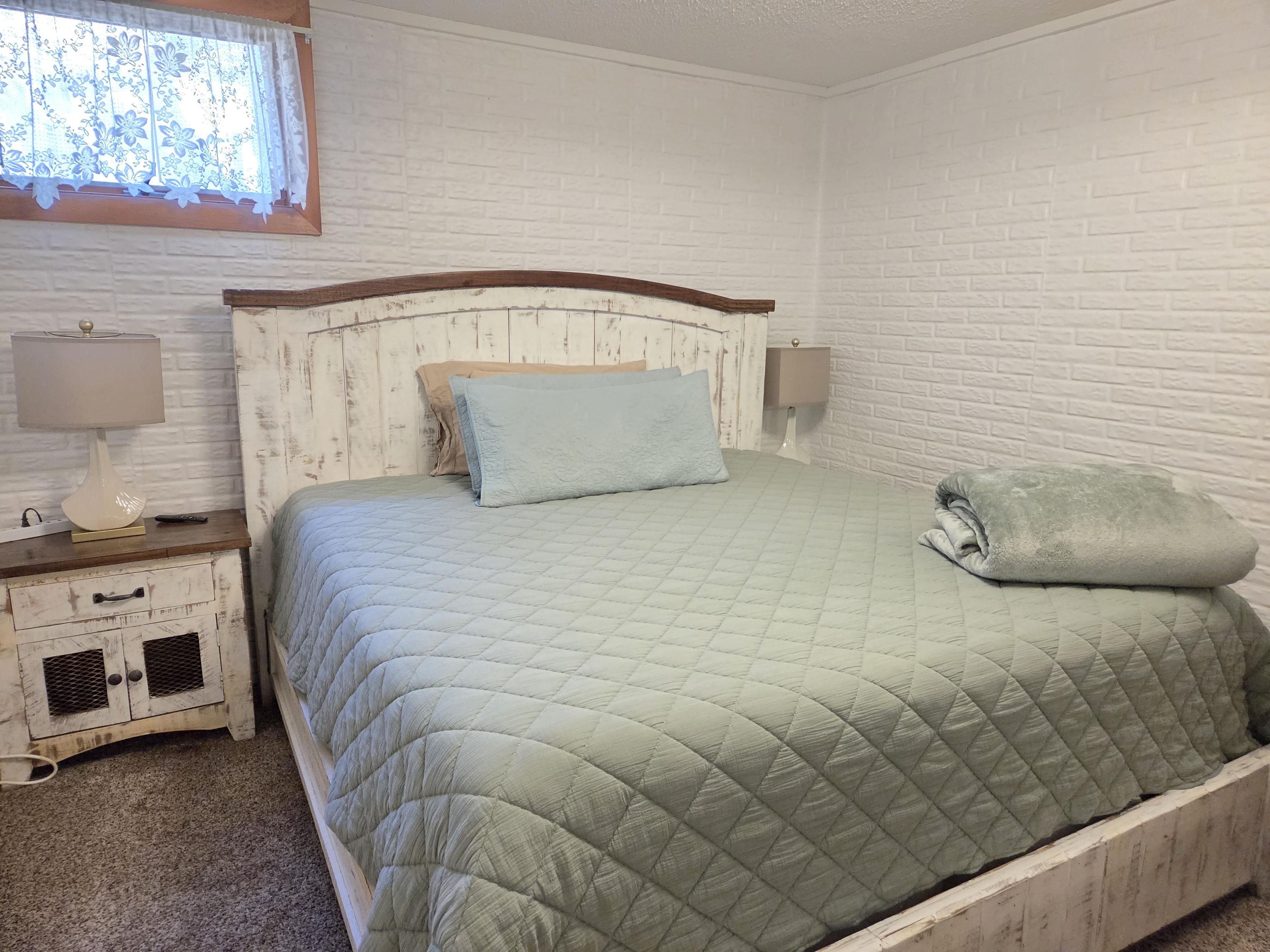 Un dormitorio con cama, mesitas de noche, lámpara y ventana con cortinas.