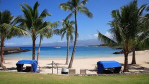 A beach with palm trees, a clear blue sky, and a boat in the water. - The Islands at Mauna Lani - Hikialani Residences B2 - Walk to beach and shops (Kamuela)