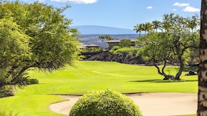 Campo de golf con vista despejada a una montaña al fondo, rodeado de exuberante vegetación y algunos edificios.