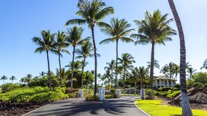 A road leading to a gated entrance with palm trees and a building in the background. - The Islands at Mauna Lani - Hikialani Residences B2 - Walk to beach and shops (Kamuela)