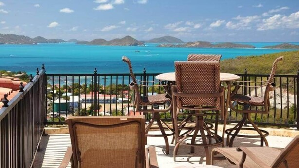 Un balcon agrémenté de fauteuils en osier et d’une table, d’où l’on peut admirer une mer turquoise et des îles lointaines.