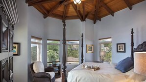 Un lit à baldaquin, un fauteuil en osier, une table de chevet avec une lampe et un plateau avec des tasses à thé.