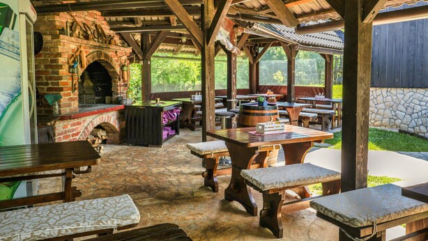 A rustic outdoor dining area with brick walls, wooden tables, and benches. - Deluxe suite in the middle of Plitvice lakes (Plitvice lakes)