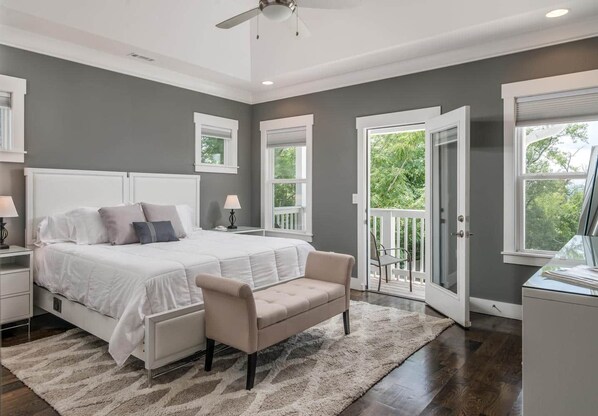 A bedroom with a large bed, a bench, a desk, and a balcony.