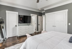 A bedroom with a large bed, a dresser, a television, and two doors.