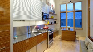 Eine moderne Küche mit Edelstahlgeräten, Holzschränken und einem großen Fenster mit Blick ins Freie.