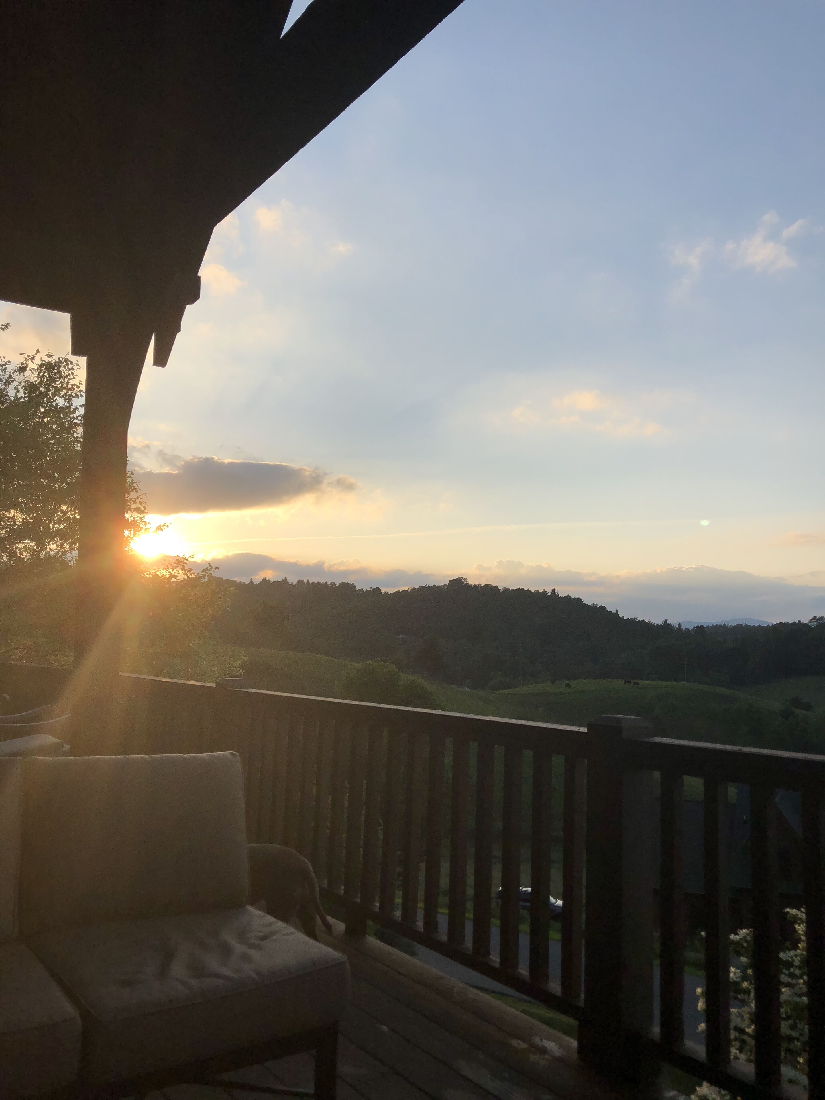 A wooden deck with a view of a sunset over a hilly landscape.