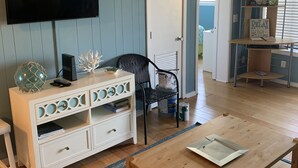 A living room with a flat-screen TV, a wooden coffee table, a white entertainment unit, a black chair, and a blue patterned rug. - The B.E.A.C.H.H.- STR Permit Number for this property is:
034944 (Hilton Head Island)