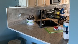 A kitchen with white cabinets, a microwave, a sink, and a countertop with stools. - The B.E.A.C.H.H.- STR Permit Number for this property is:
034944 (Hilton Head Island)