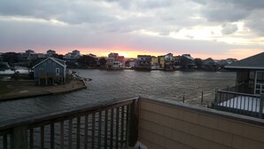 A waterfront property with a view of the sunset over the water, featuring a wooden deck and a small dock.