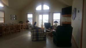 A spacious living room with a dining area, large windows, and a flat-screen TV mounted on the wall.