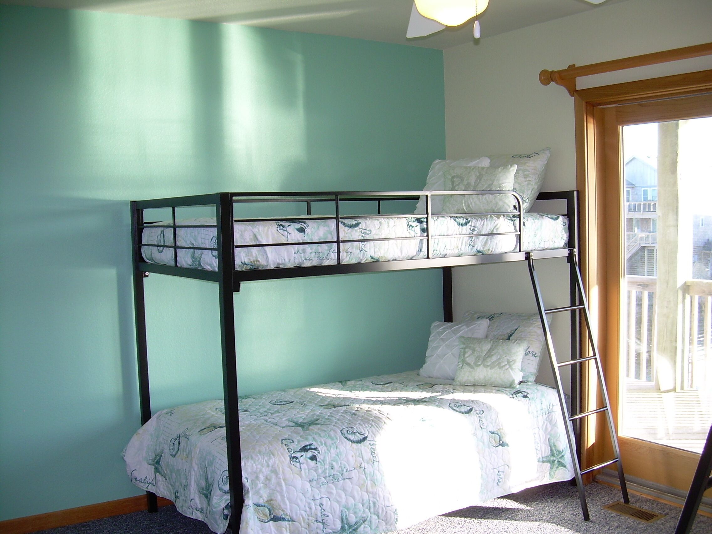 A bunk bed with a ladder, a window with a view of buildings, and a door.
