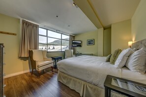 Quarto de hotel com uma cama grande, uma cadeira, escrivaninha e televisão.