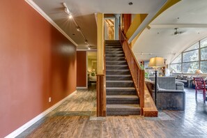 A spacious interior with a wooden staircase, a living area with a sofa and a dining table, and a large window providing natural light.