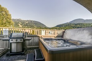 Uma varanda com banheira de hidromassagem, churrasqueira e vista para montanhas.
