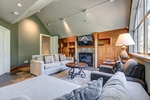 A spacious living room with a fireplace, seating area, and a television mounted on the wall.