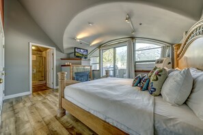 A bedroom with a large bed, a television, and a view of the outdoors through a window.