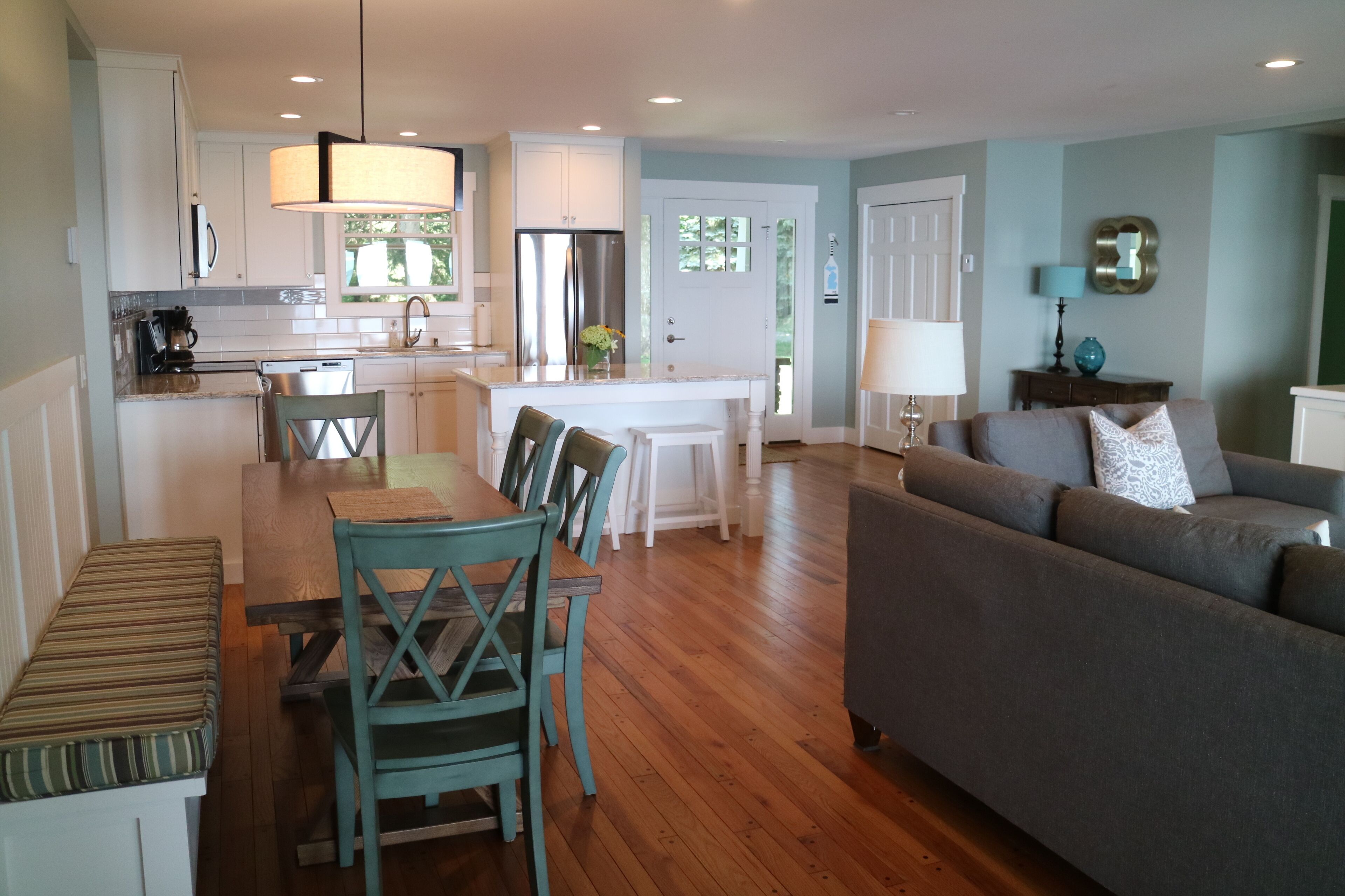 A modern kitchen with white cabinets, a stainless steel refrigerator, and a dining area with a wooden table and chairs.